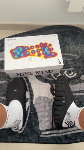 Client portant les baskets Nike Mind 001 noires, montrant la semelle striée et le dessus de la chaussure avec la boîte.