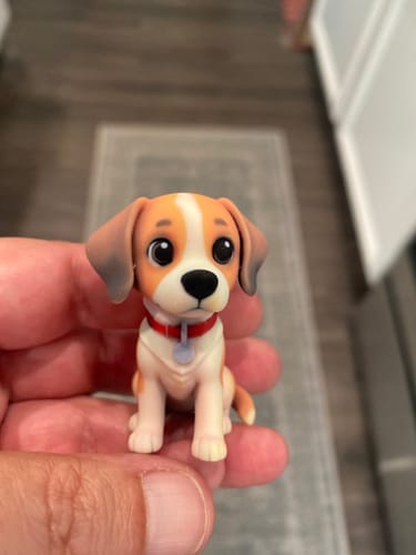 Customer's hand holding a small, cartoon-style 3D figurine of a beagle puppy with a red collar.