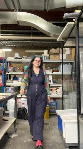 Reviewer walking through a workshop wearing the blue Yard Suit layered over a colorful long-sleeve shirt.