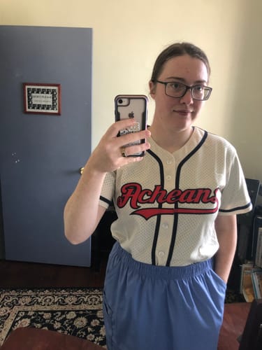 image 1 out of 3: Customer taking a mirror selfie wearing a custom cream throwback baseball jersey with red 'Achean' script on the front.