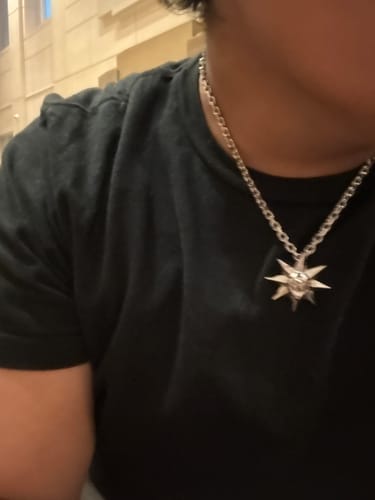Close-up of a reviewer wearing the Aries Chain with a sun-shaped pendant against a black shirt.