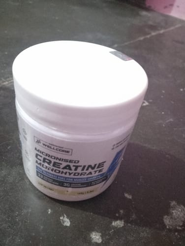 A customer's white tub of Wellcore Micronised Creatine Monohydrate on a dark surface.