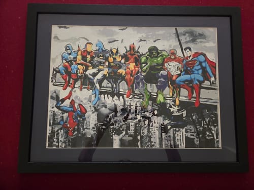 Customer's finished Custom Paint by Numbers Kit, a colorful painting of superheroes framed and hung on a wall.