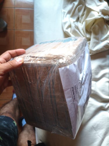 Un cliente sostiene un paquete cuadrado envuelto en plástico transparente, que contiene el producto Clomibol.