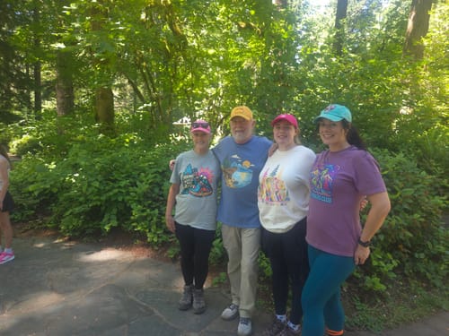 Reviewers posing in different colorful Hiking Happy T-Shirts on a wooded trail.