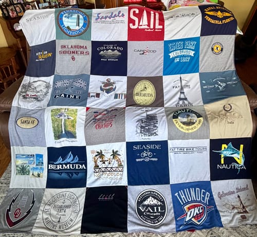 Customer's large T-Shirt Quilt draped over a couch, made from a colorful grid of memory t-shirts from travels and teams.