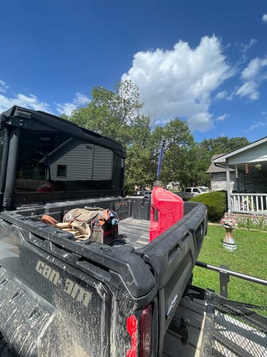 Customer's red 5 Gallon Jug sitting in the bed of a muddy Can-Am utility vehicle on a sunny day.