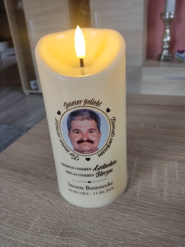 Kunde zeigt seine leuchtende, personalisierte LED-Gedenkkerze mit einem Foto und Trauersprüchen auf einem Holztisch.