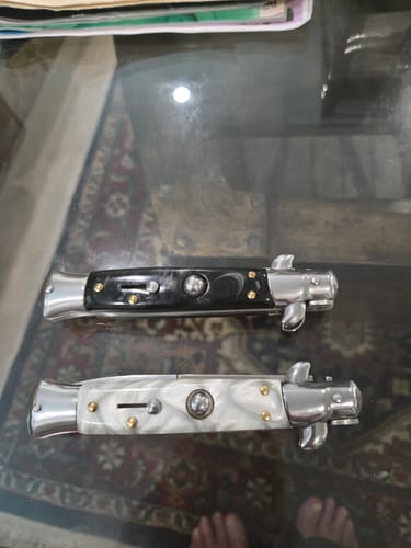 Reviewer's black and white marble Italian Style Push Button Switchblades shown closed on a glass table.