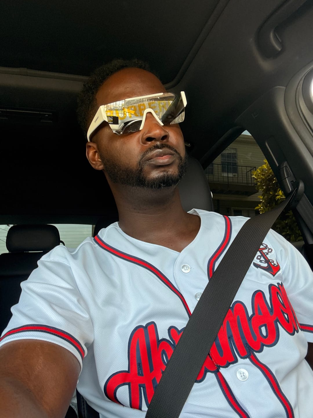 Customer wearing a white custom baseball jersey with red script and trim, seen from inside a car.