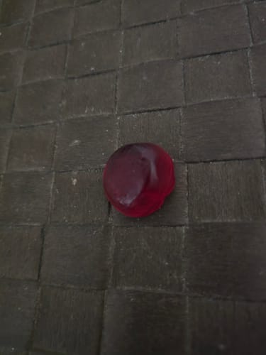 Kundenfoto eines einzelnen roten THC Spacejellies 2.0 Gummibärchens auf einer dunklen, gewebten Oberfläche.