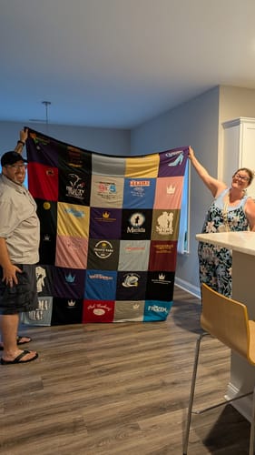 Customers holding up their completed Project Repat T-Shirt Quilt made of many colorful t-shirt squares.