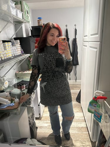 Reviewer taking a mirror selfie while wearing a black patterned apron from the Mystery Box.