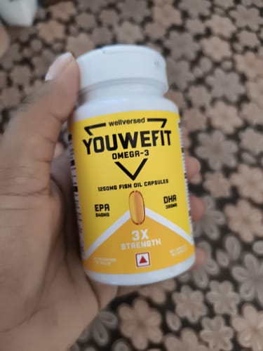 Customer's hand holding the white bottle of YouWeFit Omega-3 Fish Oil with its bright yellow label.