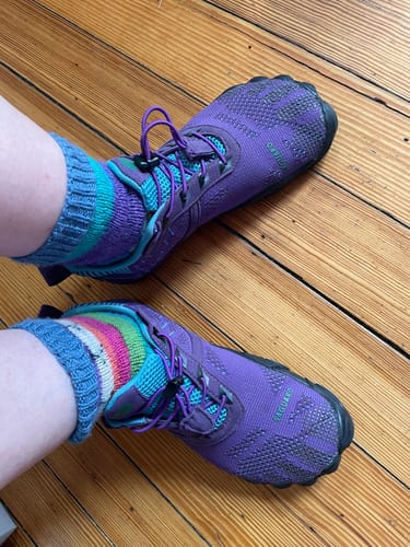 A customer wearing purple Free I - Barefoot Shoes with colorful socks on a wooden floor.