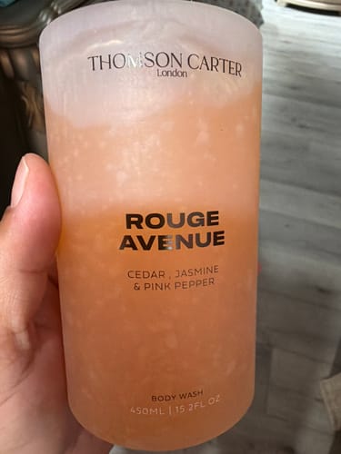 Customer holding the frosted bottle of Rouge Avenue Body Wash, showing the peach-colored liquid inside.