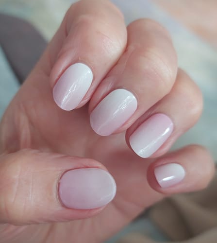 Hand einer Kundin, die die UV-Nagelfolien „Blush Radiance“ mit einem sanften, rosa-weißen Farbverlauf trägt.