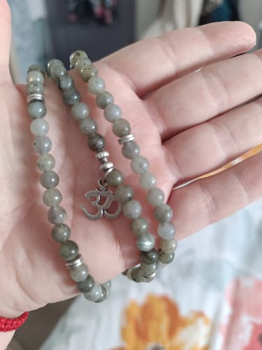 Un client tient dans sa main le bracelet mala en Labradorite enroulé, montrant les perles grises et le médaillon Om.