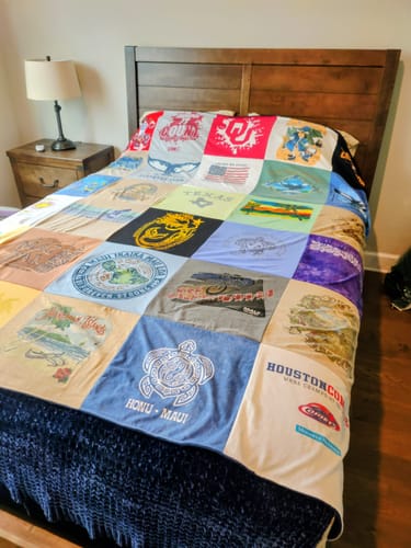 Customer's Project Repat T-Shirt Quilt made from memorial shirts, spread neatly across a bed.