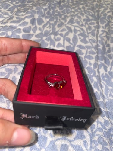 Customer holding the black jewelry box open to show the MINI PROMISE RING with a red heart-shaped stone.
