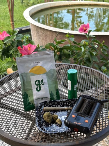 Customer's bag of Blue Dream, loose buds, a joint, and a vaporizer on a small tray outdoors.