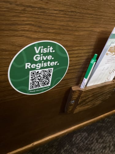 Customer's green custom sample sticker with a QR code on a wooden church pew.