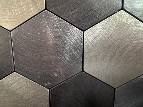 Kundens nærbilde av Latte hexagon selvklebende veggfliser med små, runde misfarginger på overflaten.