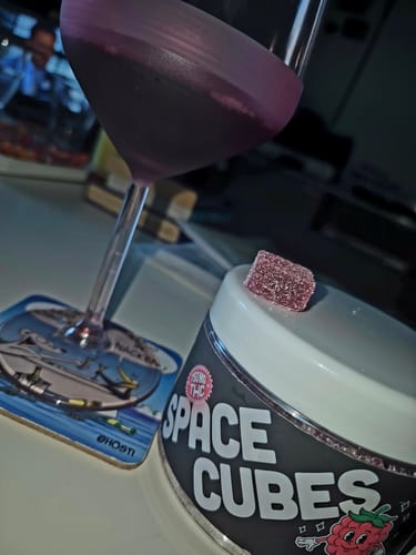 Ein Kunde zeigt einen einzelnen lila THC Space Cube auf der Dose neben einem Glas.
