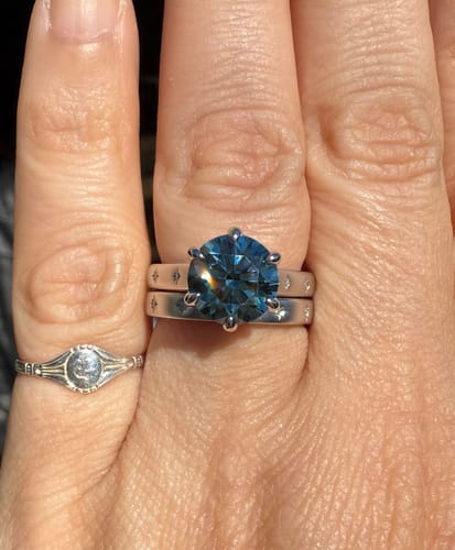Reviewer's hand wearing the custom wedding band, shown as a set with a large blue stone ring.