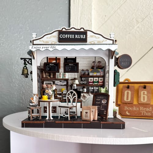 A customer's completed Coffee Stop DIY kit, a detailed miniature cafe with outdoor seating and a small cat figure.