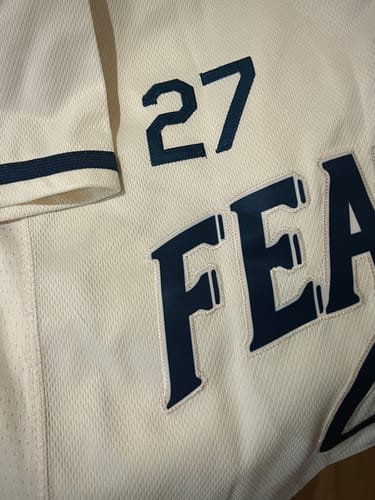 Close-up of a customer's custom cream baseball jersey showing the navy stitched lettering and number 27.