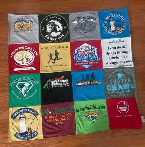 Customer's Project Repat T-Shirt Quilt made from various running race shirts, laid out flat on a wood floor.