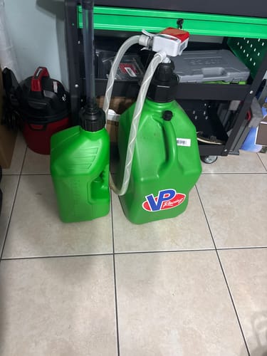 Reviewer's green 2.5 Gallon Auto Stop Jug shown next to a larger jug for a size comparison in a garage.