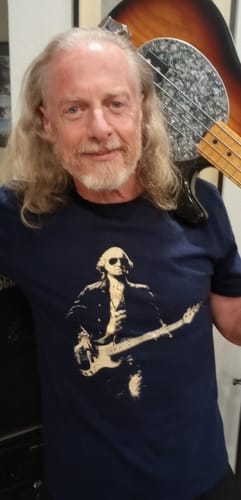 Reviewer wearing the dark Washington Bass Face T-Shirt while holding a bass guitar over their shoulder.