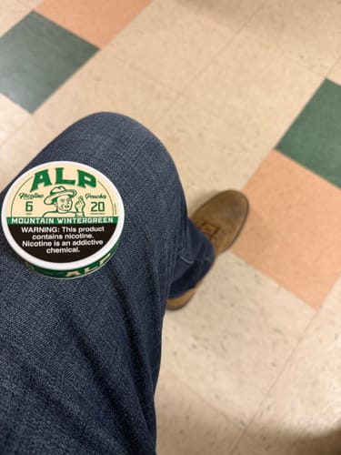 Customer's can of Mountain Wintergreen Nicotine Pouches resting on their jean-clad leg in a waiting area.