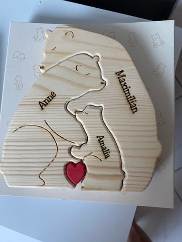 Ein Kunde zeigt ein personalisiertes Bärenpuzzle aus Holz, das eine Familie mit drei Bären und einem roten Herz darstellt.