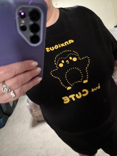 Reviewer in a mirror selfie showing the fit of the black 'Anxious But Cute' T-shirt.