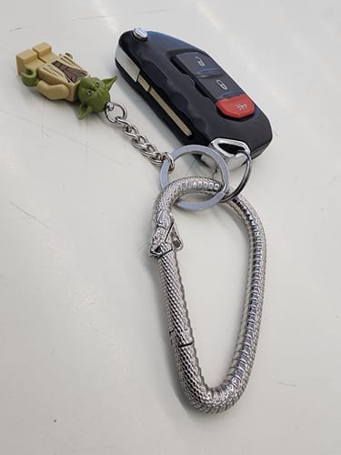Customer's silver Ouroboros Carabiner attached to a car key fob and a character keychain on a white surface.