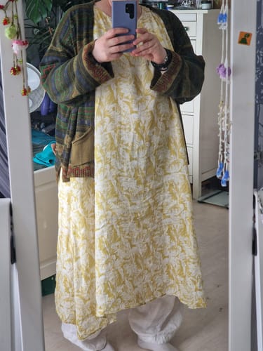 Reviewer in a mirror selfie showing the drape of the yellow floral Artsy Vest Dress, worn with a cardigan.