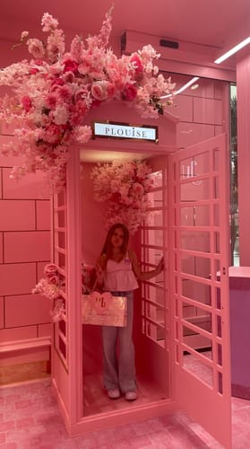 Customer's daughter posing in a pink, flower-decorated telephone booth during her Walk In experience.
