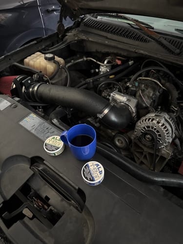 Customer's two tins of Chilled Mint Nicotine Pouches and a blue mug of coffee resting on a car engine.