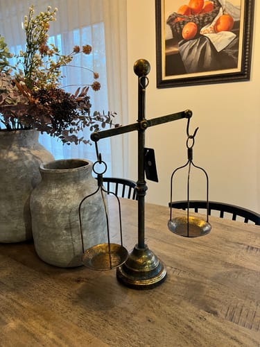 Customer's aged gold Salomon Balance Scale Candle Holder displayed on a wooden table with the tag still on.