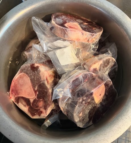 Customer's frozen Beef Shank portions in vacuum-sealed packages, sitting in a large metal pot.