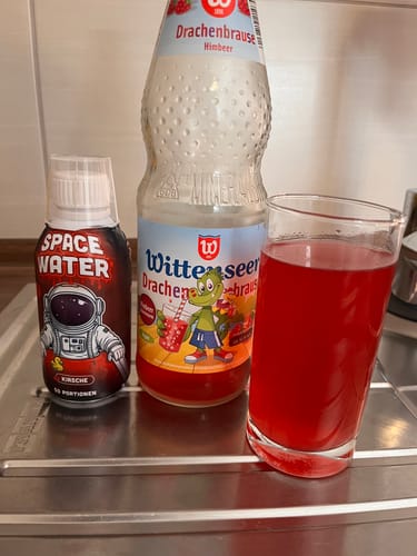 Ein Kunde zeigt seinen Spacewater THC-Sirup (Kirsche) neben einem Glas mit dem fertigen roten Getränk.