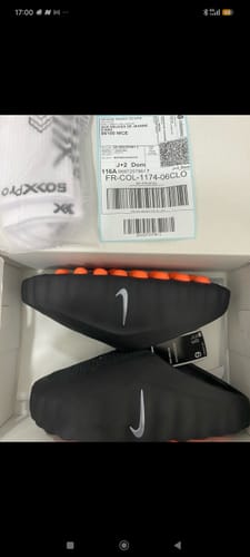 Client montrant les chaussures Nike Mind 001 noires avec la semelle orange, dans leur boîte.
