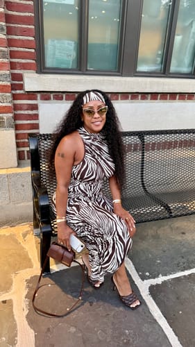 Reviewer sitting on a bench outdoors, styled in the zebra-print Naked Print Sleeveless Midi Dress with matching accessories.