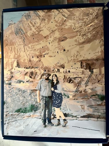 Customer's completed Custom Paint By Numbers portrait of a couple in front of a large cliff dwelling.