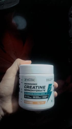 Reviewer holding a white tub of Wellcore Micronised Creatine Monohydrate in the Tropical Tango flavor.