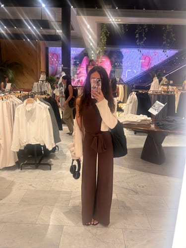 Reviewer in a store wearing the brown Smooth Halter Wide-Leg Jumpsuit with the neck straps tied around her waist as a belt.