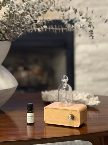 Reviewer's Aura Nebulizer with a light wood base and glass top, sitting on a dark wood table.
